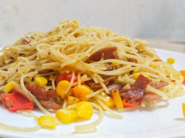 Homemade recipe classic aglio e olio pasta with smoked beef and corn, close-up in a white plate on the table clipart