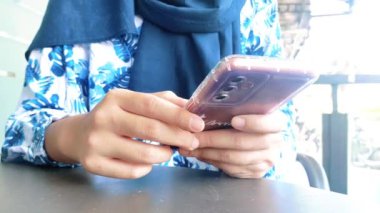 Gündüz vakti cep telefonuyla yazı yazıp sohbet eden bir kadının ellerini yakın plan çekiyoruz.