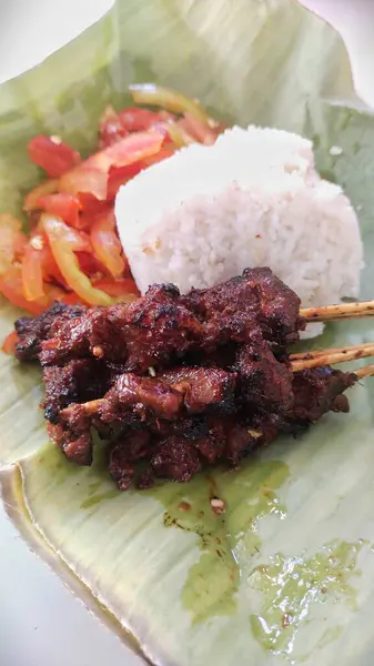 stock image street food, goat satay served with tomato sambal and white rice on banana leaves