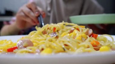 Bir kadın aglio e olio spagetti yiyor evde füme sığır eti ve rendelenmiş mısırla tarifi yapıyor.