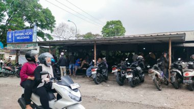 Bandung, Endonezya - 2 Ekim 2024; Geleneksel gıda tezgahına park etmiş insan ve motosiklet kalabalığı uygun fiyatlı ev yemeği sağlıyor