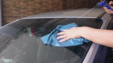 Evde arabanın ön camını yıkamak için su püskürtme hortumu ve bukleli bez kullanmak.