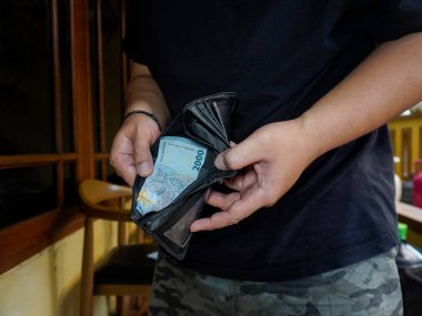 Bandung, Endonezya - 20 Ekim 2024; Cüzdanının boş olduğunu fark eden bir adamın yakın çekimi sadece 2.000 Endonezya Rupiah notu içerir