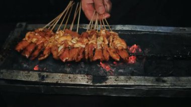 Endonezya 'dan gelen sokak yemekleri, geleneksel kömür ateşinde satay tavuğu çok fazla dumana neden oluyor. Eller ızgarada satay pişiriyor.