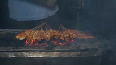 Endonezya 'dan gelen sokak yemekleri, geleneksel kömür ateşinde satay tavuğu çok fazla dumana neden oluyor. Eller ızgarada satay pişiriyor.