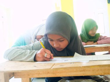 Bandung, Endonezya - 29 Mart 2022; kadın bir İslami yatılı okul öğrencisi OMR kağıdındaki sınav sorularını cevaplamaya odaklanmıştır.