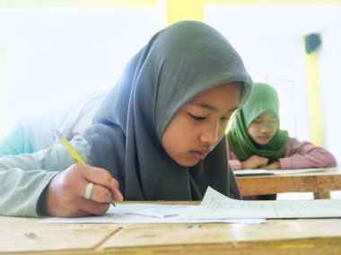 Bandung, Endonezya - 29 Mart 2022; kadın bir İslami yatılı okul öğrencisi OMR kağıdındaki sınav sorularını cevaplamaya odaklanmıştır.