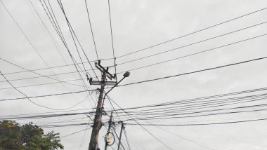 Bulutlu gökyüzünün altında elektrik kabloları olan elektrik direkleri.