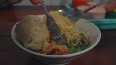 Bandung, Endonezya - 6 Şubat 2025; tezgahtaki kasede köfte çorbası (Bakso) yemek. Endonezya 'nın geleneksel sokak yemeklerinden biridir. Erişte çorbası ve köftelerden oluşur.