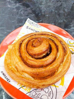 Tatlı tarçınlı rulo kırmızı tabakta cam masanın üstünde