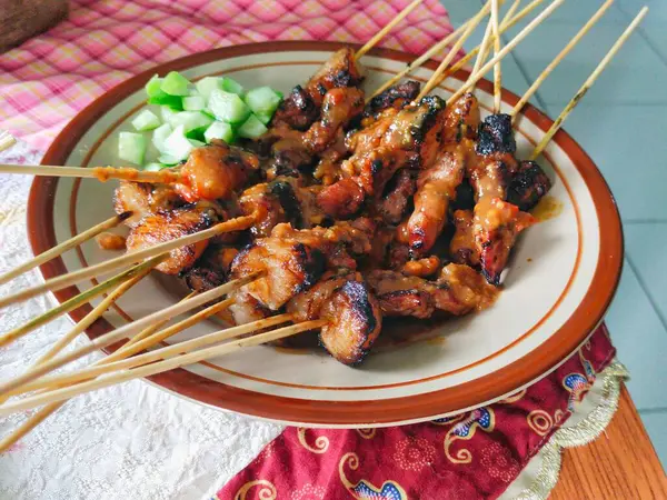 Masadaki tabakta salatalık turşusuyla servis edilen Endonezya sığır eti satayı. Sate sapi 