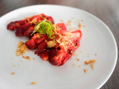 Lezzetli bir Çin yemeği, Char Siu Chicken veya kızarmış Char Siu Chicken veya Char Siew, kırmızı mayalı pirinçten yapılmış parlak kırmızı bir tavuk. Tahta bir masada beyaz bir tabakta servis edilir. Seçici odak