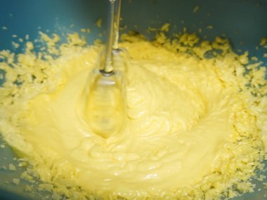 Mangırı bir kasede karıştırıyor, el çırpıcısı kullanıyor, yakınlaştırıyor.