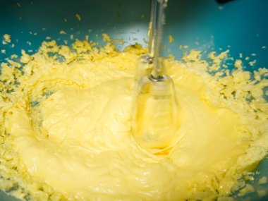 Mangırı bir kasede karıştırıyor, el çırpıcısı kullanıyor, yakınlaştırıyor.