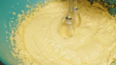 Mangırı bir kasede karıştırıyor, el çırpıcısı kullanıyor, yakınlaştırıyor.