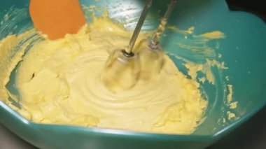 Mangırı bir kasede karıştırıyor, el çırpıcısı kullanıyor, yakınlaştırıyor.