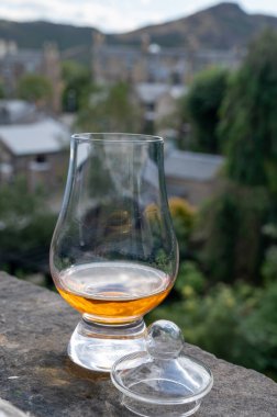 Glass of single malt scotch whisky served on old window sill in Scottisch house with view on old part of Edinburgh city, Scotland, UK, dram of blended whiskey