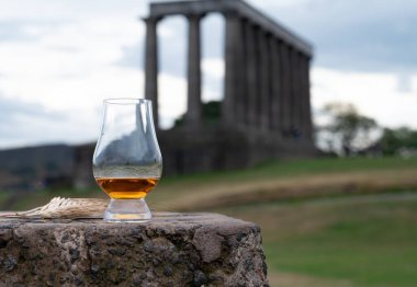 Glass of single malt scotch whisky and view from Calton hill to park and old parts of Edinburgh city in rainy summer day, Scotland, UK