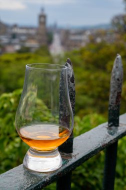 Glass of single malt scotch whisky and view from Calton hill to park and old parts of Edinburgh city in rainy summer day, Scotland, UK