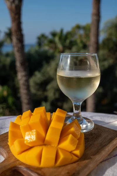 stock image Fresh ripe sweet yellow mango tropical fruit served outdoor with glass of cold white wine and view on green palm trees and blue sea