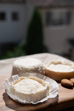 Fransız peynirleri Rocamadour ve Saint-Marcellin güneş ışığında bademlerle zeytin ağacı tahtasında servis edildi.