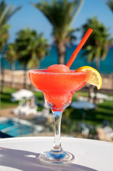 Colourful frozen pink Strawberry daiquiri cocktail drink served in glass at outdoor cafe overlooking blue sea and palm trees, relax and holidays at sea