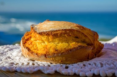 Portugeese homemade oven baked yellow corn bread served outdoor with view on blue Atlantic ocean in Lisbon area, Portugal, close up clipart