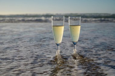 Kava bardakları ya da şampanya beyaz kumlu okyanus sahilinde köpüklü şarap. Gün batımında gölgeli güneş dalgaları.