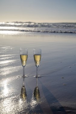 Kava bardakları ya da şampanya beyaz kumlu okyanus sahilinde köpüklü şarap. Gün batımında gölgeli güneş dalgaları.