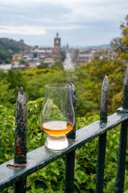 Glass of single malt scotch whisky and view from Calton hill to park and old parts of Edinburgh city in rainy summer day, Scotland, UK