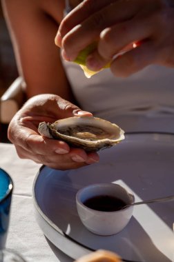 Beyaz elbiseli genç kadın taze kremalı istiridye ve limon suyu yiyor, Fransız restoranında deniz ürünleri yiyor.