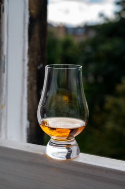 Glass of single malt scotch whisky served on old window sill in Scottisch house with view on old part of Edinburgh city, Scotland, UK, dram of blended whiskey