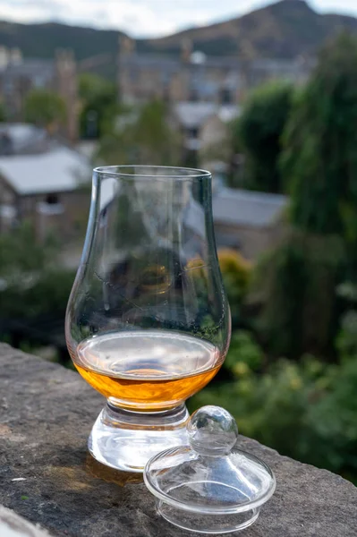 Glass of single malt scotch whisky served on old window sill in Scottisch house with view on old part of Edinburgh city, Scotland, UK, dram of blended whiskey