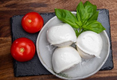 Beyaz İtalyan yumuşak peyniri Mozzarella di Bufala Campana topları taze yeşil fesleğen yaprakları ve kırmızı domatesle servis edilir.