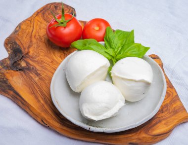 Beyaz İtalyan yumuşak peyniri Mozzarella di Bufala Campana topları taze yeşil fesleğen yaprakları ve kırmızı domatesle servis edilir.