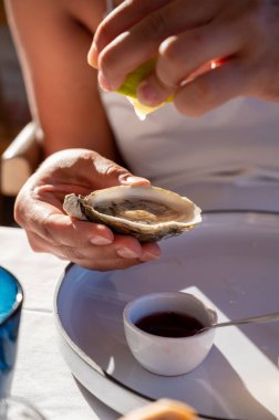 Beyaz elbiseli genç kadın taze kremalı istiridye ve limon suyu yiyor, Fransız restoranında deniz ürünleri yiyor.