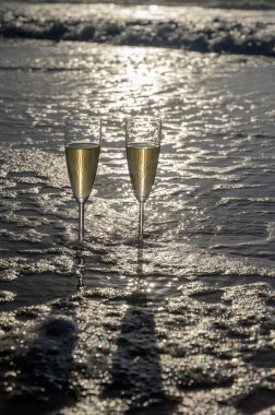 Kava bardakları ya da şampanya beyaz kumlu okyanus sahilinde köpüklü şarap. Gün batımında gölgeli güneş dalgaları.