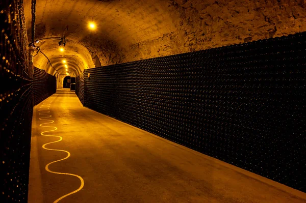 Walking in deep long undergrounds caves with dusty bottles on racks, making champagne sparkling wine from chardonnay and pinor noir grapes in Epernay, Champagne, France