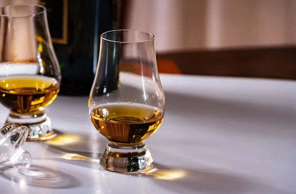 Tasting of whiskey, tulip-shaped tasting glasses with dram of Scotch single malt or blended whisky on white table, close up
