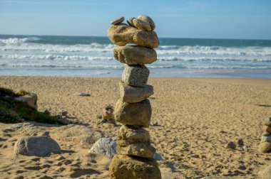 Günbatımında kumlu sahilde, dengeli taşlardan oluşan piramit, Atlantik Okyanusu, Portekiz