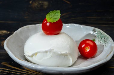 Büyük bir top yumuşak beyaz İtalyan mozzarella bufala campania peyniri üzerinde kırmızı domates ve yeşil fesleğen yapraklı siyah taş tabakta