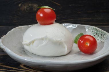 Büyük bir top yumuşak beyaz İtalyan mozzarella bufala campania peyniri üzerinde kırmızı domates ve yeşil fesleğen yapraklı siyah taş tabakta