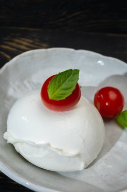Büyük bir top yumuşak beyaz İtalyan mozzarella bufala campania peyniri üzerinde kırmızı domates ve yeşil fesleğen yapraklı siyah taş tabakta