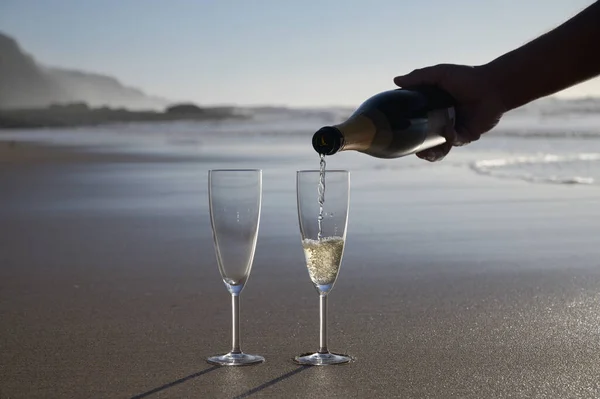Pouring of cava or champagne sparkling white wine on white sandy ocean beach on sunset in sunlights