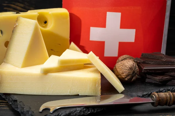 stock image Assortment of Swiss cheeses Emmental or Emmentaler medium-hard cheese with round holes, Gruyere, appenzeller used for traditional cheese fondue and gratin and flag of Switzerland on dark background