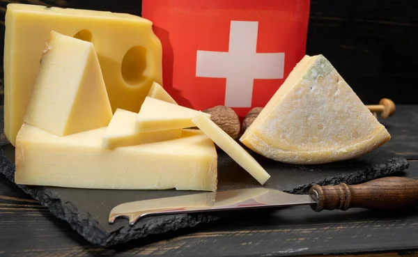 Assortment of Swiss cheeses Emmental or Emmentaler medium-hard cheese with round holes, Gruyere, appenzeller used for traditional cheese fondue and gratin and flag of Switzerland on dark background