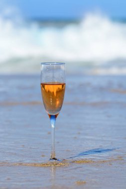 One glass of rose champagne or cava sparkling wine served on white sandy tropical beach and blue ocean water, romantic vacation, winter sun on Fuerteventura, Canary, Spain