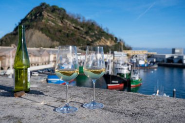 Tasting of txakoli or chacoli slightly sparkling very dry white wine produced in Spanish Basque Country with view on old port and sunny village Getaria, Spain