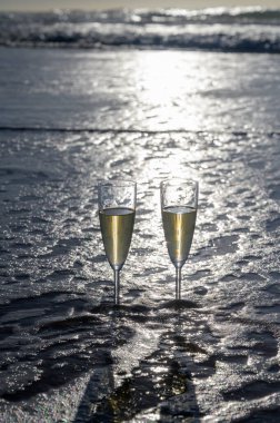 Kava bardakları ya da şampanya beyaz kumlu okyanus sahilinde köpüklü şarap. Gün batımında gölgeli güneş dalgaları.