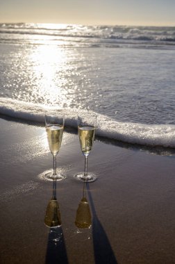 Kava bardakları ya da şampanya beyaz kumlu okyanus sahilinde köpüklü şarap. Gün batımında gölgeli güneş dalgaları.